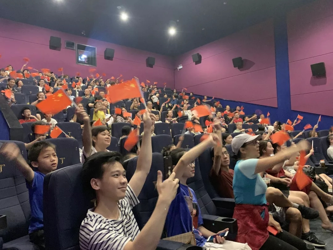 广州某影厅,观众挥舞国旗等待直播开始。